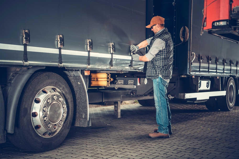 Truck driver standing beside his semi trailer performing a pre-trip inspection