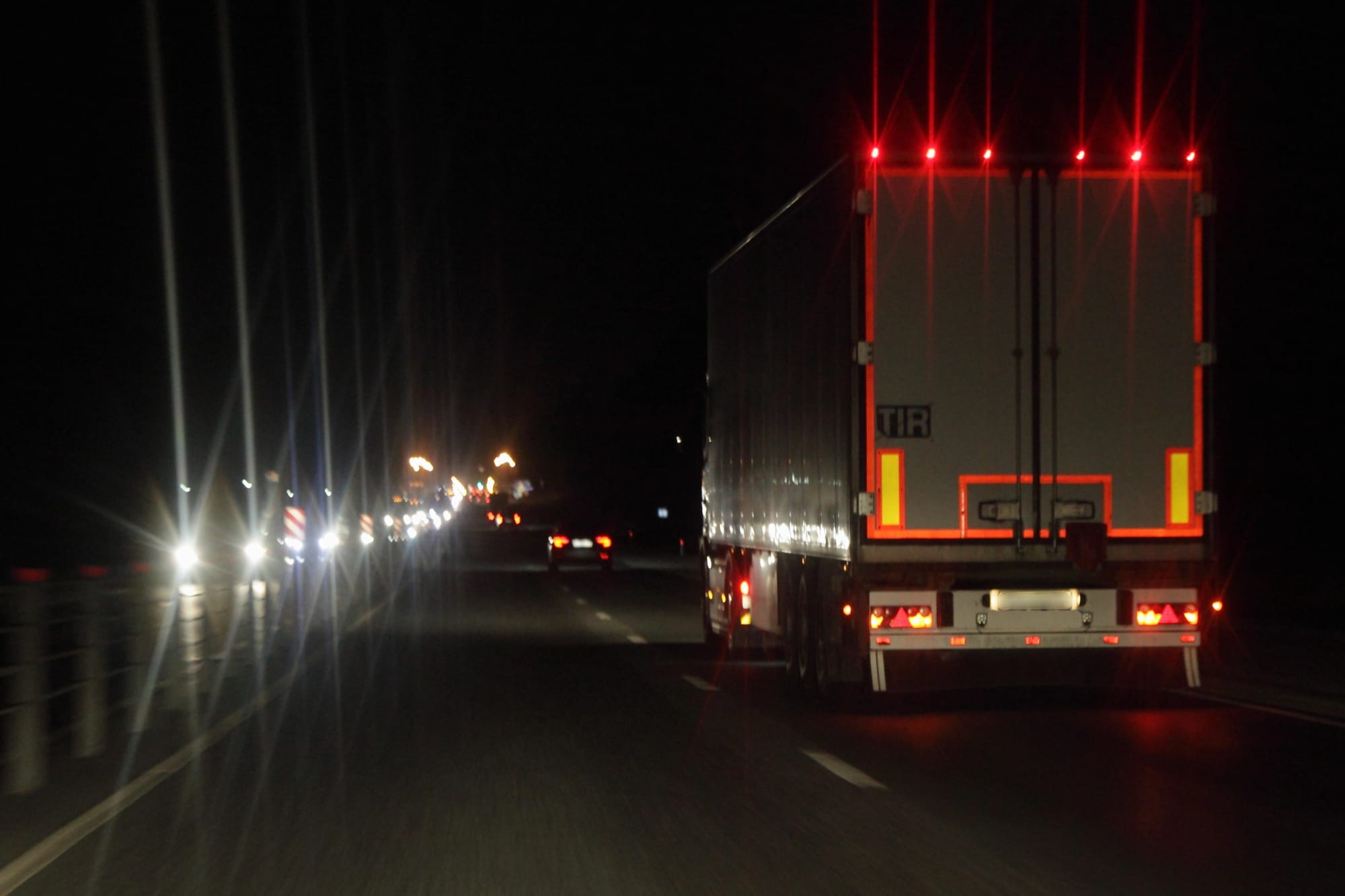Commercial truck driving on highway at night with headlights and reflective safety markings, illustrating AI dash cams for fleets and predictive collision prevention.