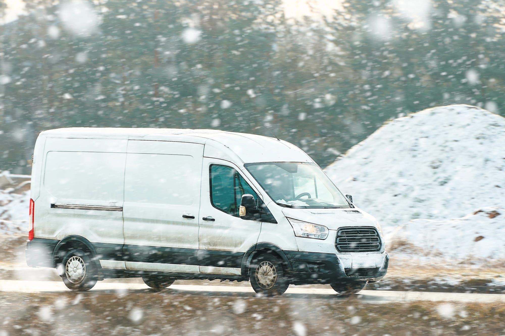 White delivery van driving through snowstorm, illustrating winter weather intelligence for fleet safety.